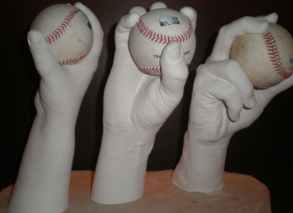 Three white hand sculptures holding baseballs, showcasing the art of handcasting for capturing baseball grips in detailed sculptures.