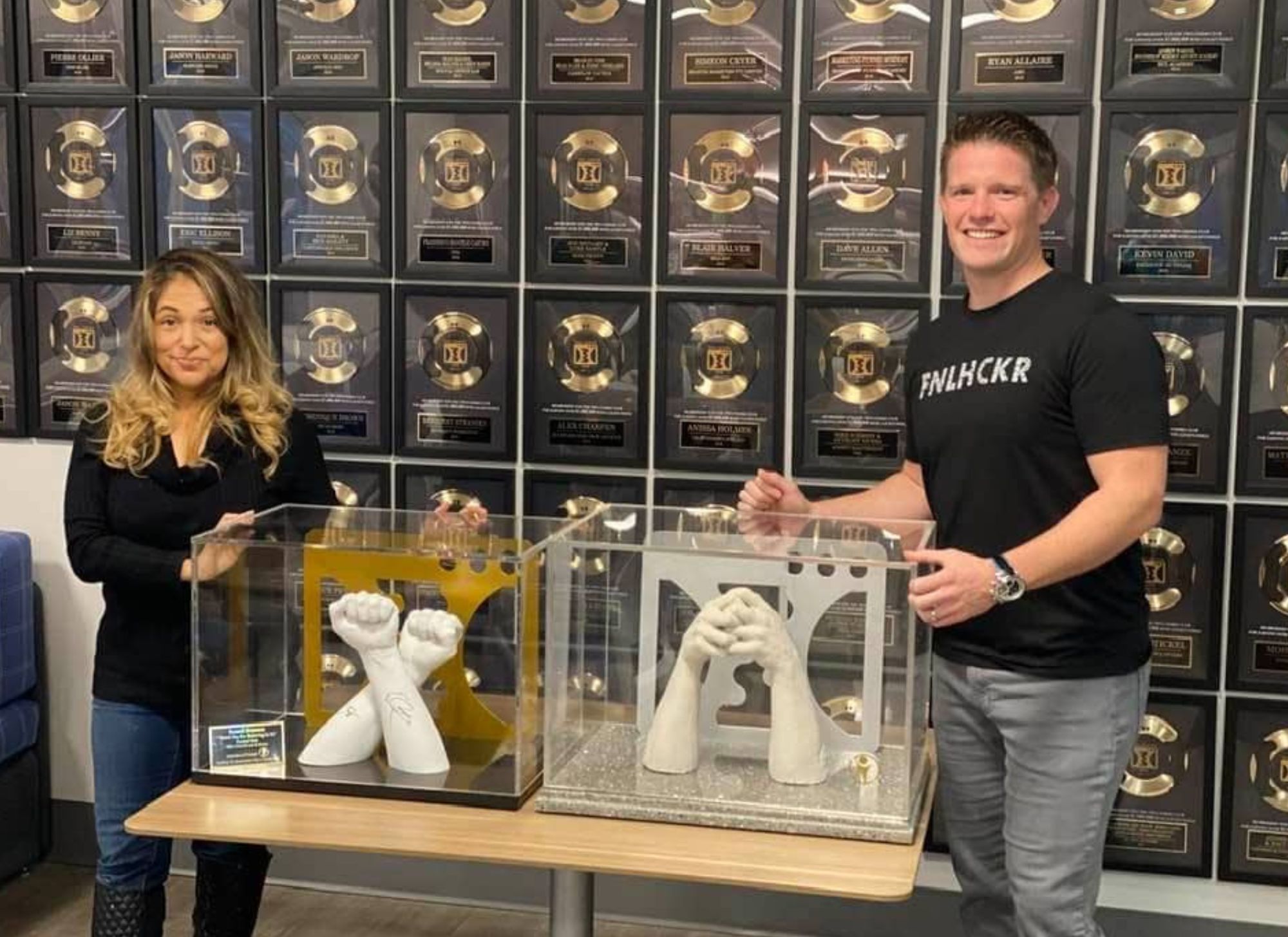 Russell Brunson, owner of ClickFunnels, showcasing custom hand sculptures inspired by the ClickFunnels logo, displayed alongside the One Comma Club awards.