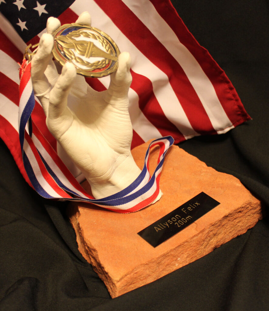 Hand sculpture of Allyson Felix holding a gold medal, crafted by Grace Irene, celebrating her legendary achievements in track and field.