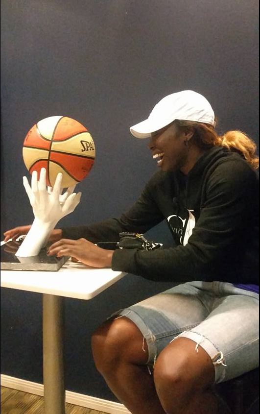 Essence Carson observing a hand-cast sculpture holding a basketball, symbolizing the emotional value of sports memories captured through hand casting.