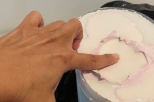 Hand presses into molding material inside a bucket as the mold forms around the fingers