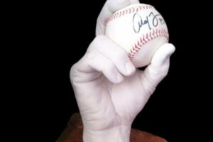 White handcast sculpture holds a signed baseball against a dark background on a stone base