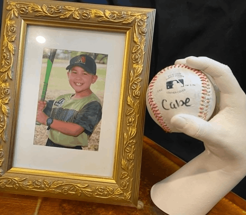 Finished personalized baseball gift — hand-cast plaster grip holding a baseball next to a framed childhood photo
