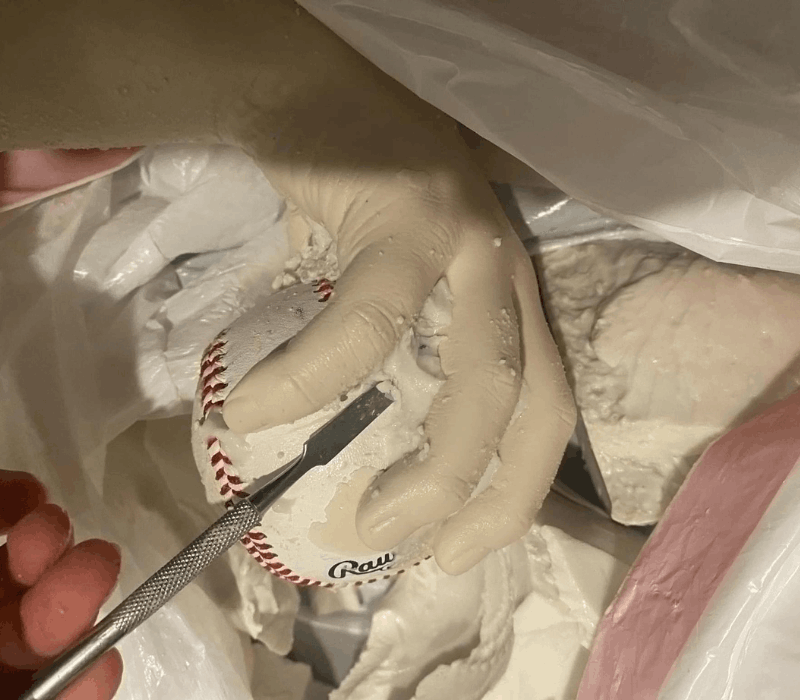 Close-up of a plaster baseball hand cast gripping a real Rawlings baseball, hand-finished with detailing tool by Grace at Keepsakes of Triumph